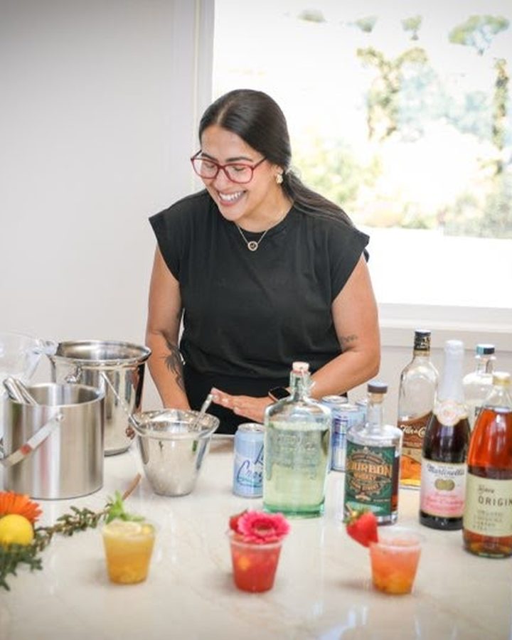Marcella muddling fresh ingredients beside a row of colorful craft cocktails