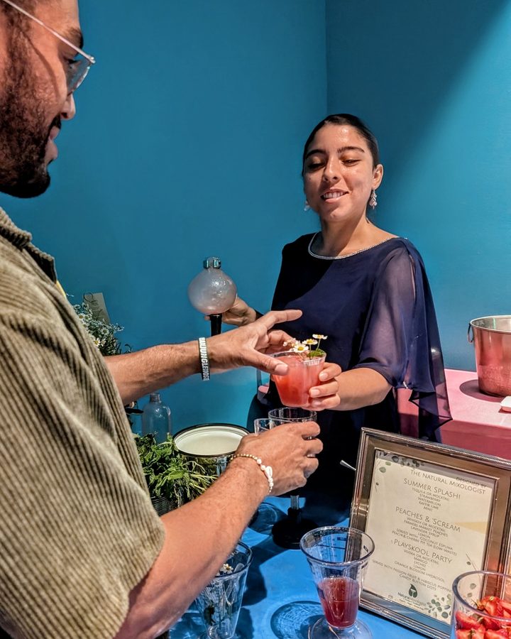 A Natural Mixologist team member handing a guest a fresh fruit cocktail